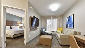 A hotel room with a bed, a sofa, a small table, a TV, and a window with curtains. - Staybridge Suites Waterloo - St. Jacobs Area by IHG (Township of Woolwich)