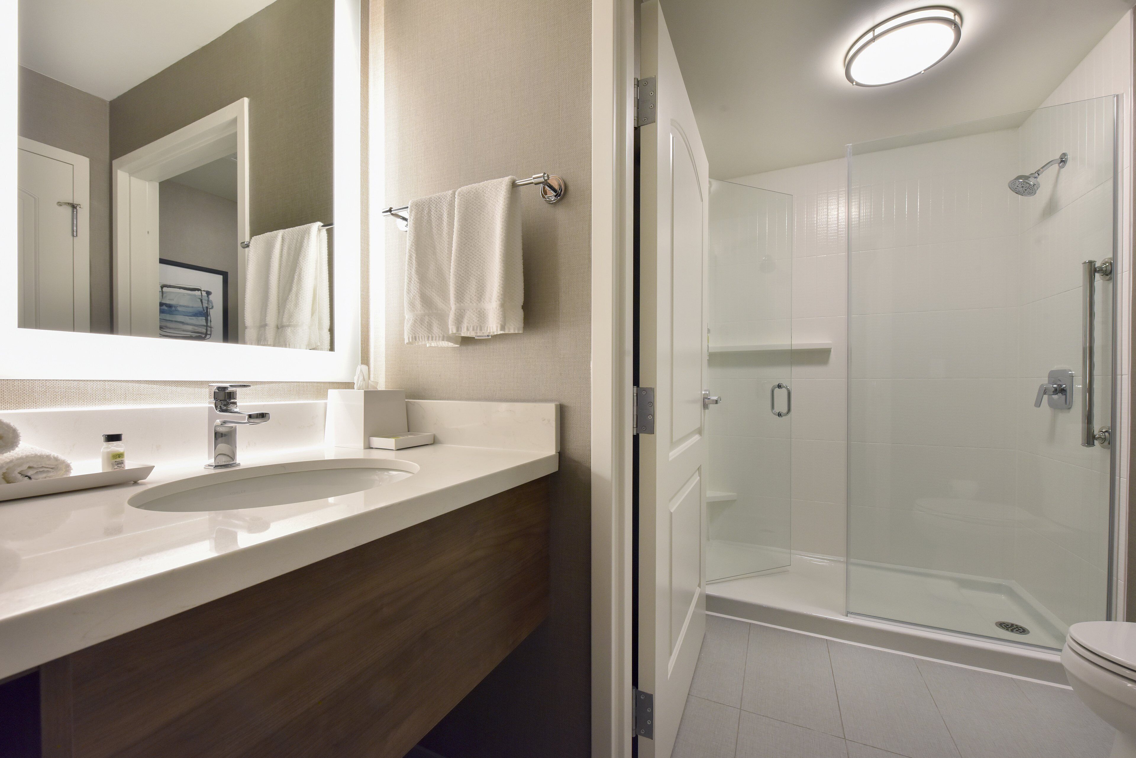 A modern bathroom with a large mirror, a sink, a glass-enclosed shower, and a toilet.