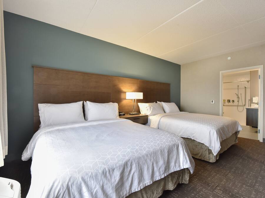 Habitación de hotel con dos camas, una mesita de noche, una lámpara y un baño visible a través de una puerta abierta.