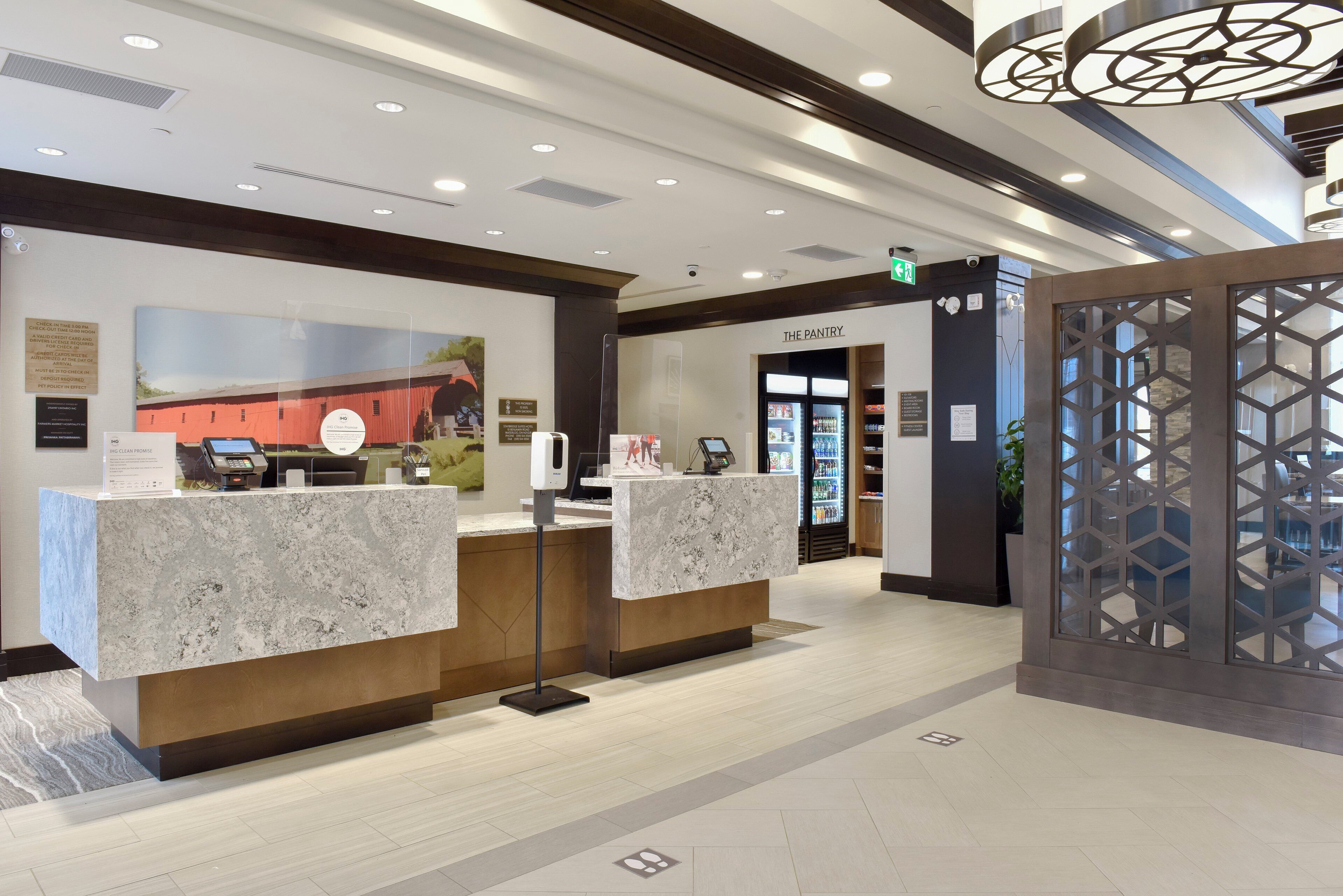 A reception area with marble counters, a digital check-in kiosk, and a sign for 'The Pantry' in the background.