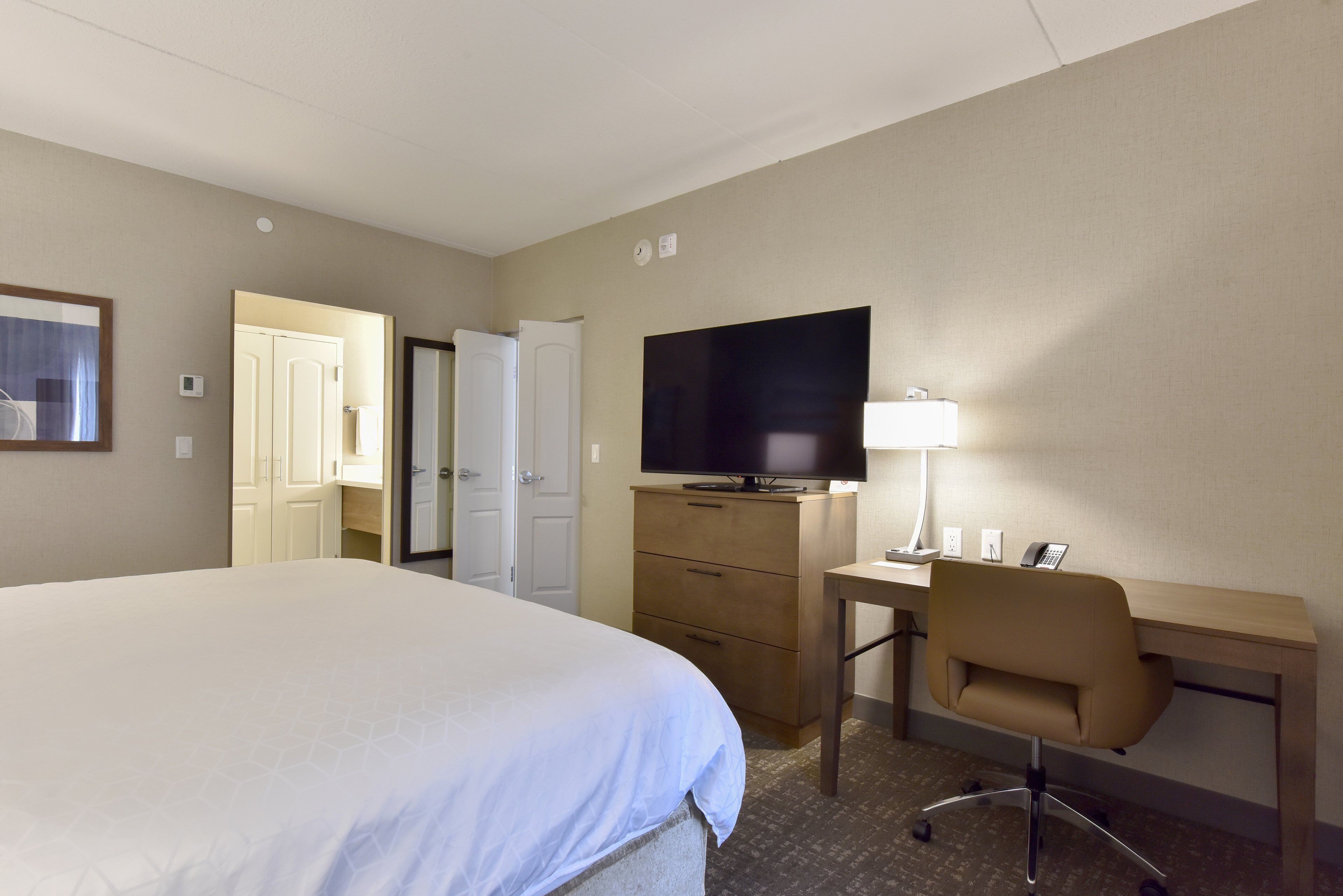 A hotel room with a large bed, a desk with a chair, a television, and a lamp.