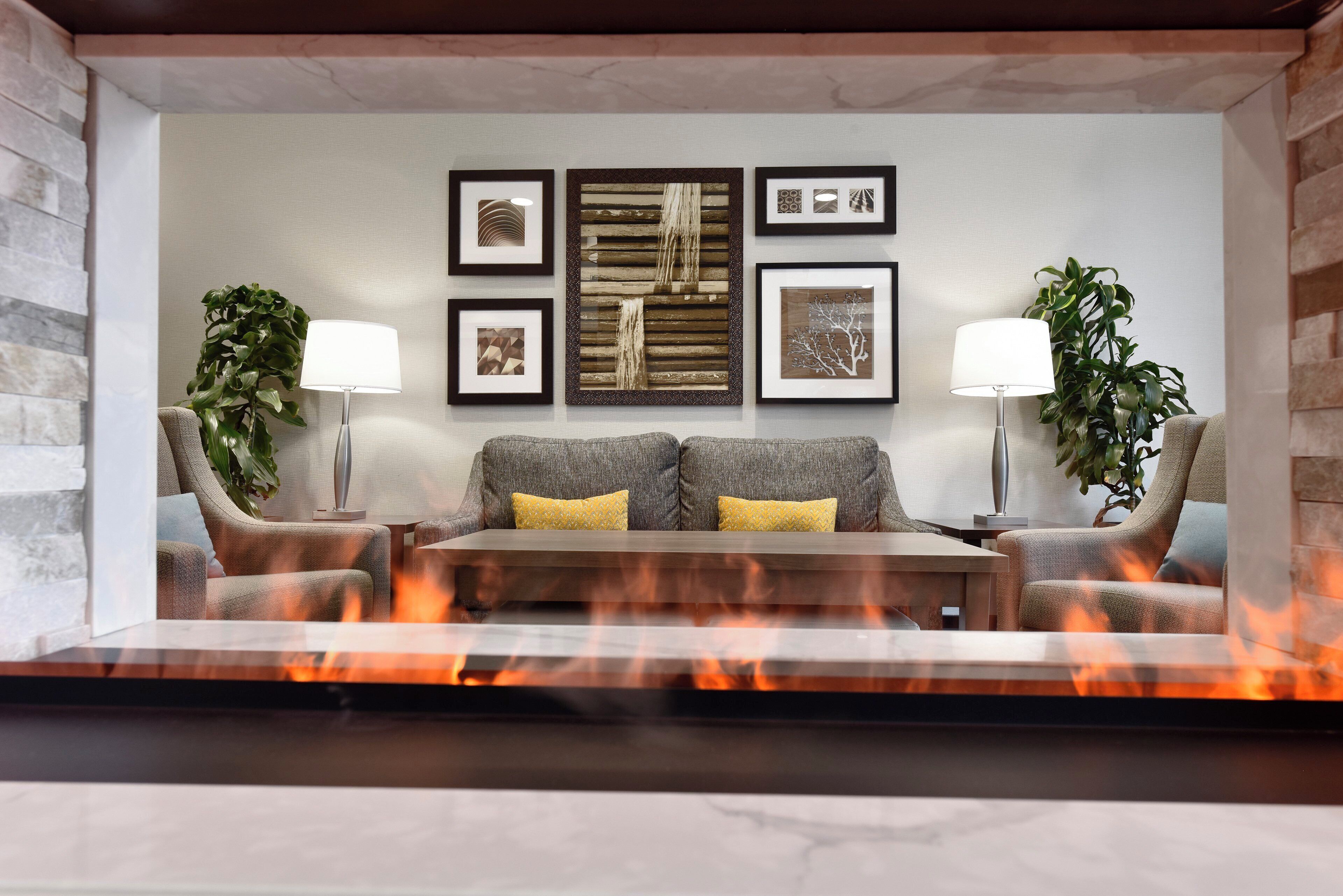 Ein modernes Wohnzimmer mit Kamin, grauem Sofa, zwei Sesseln und gerahmten Kunstwerken an der Wand.