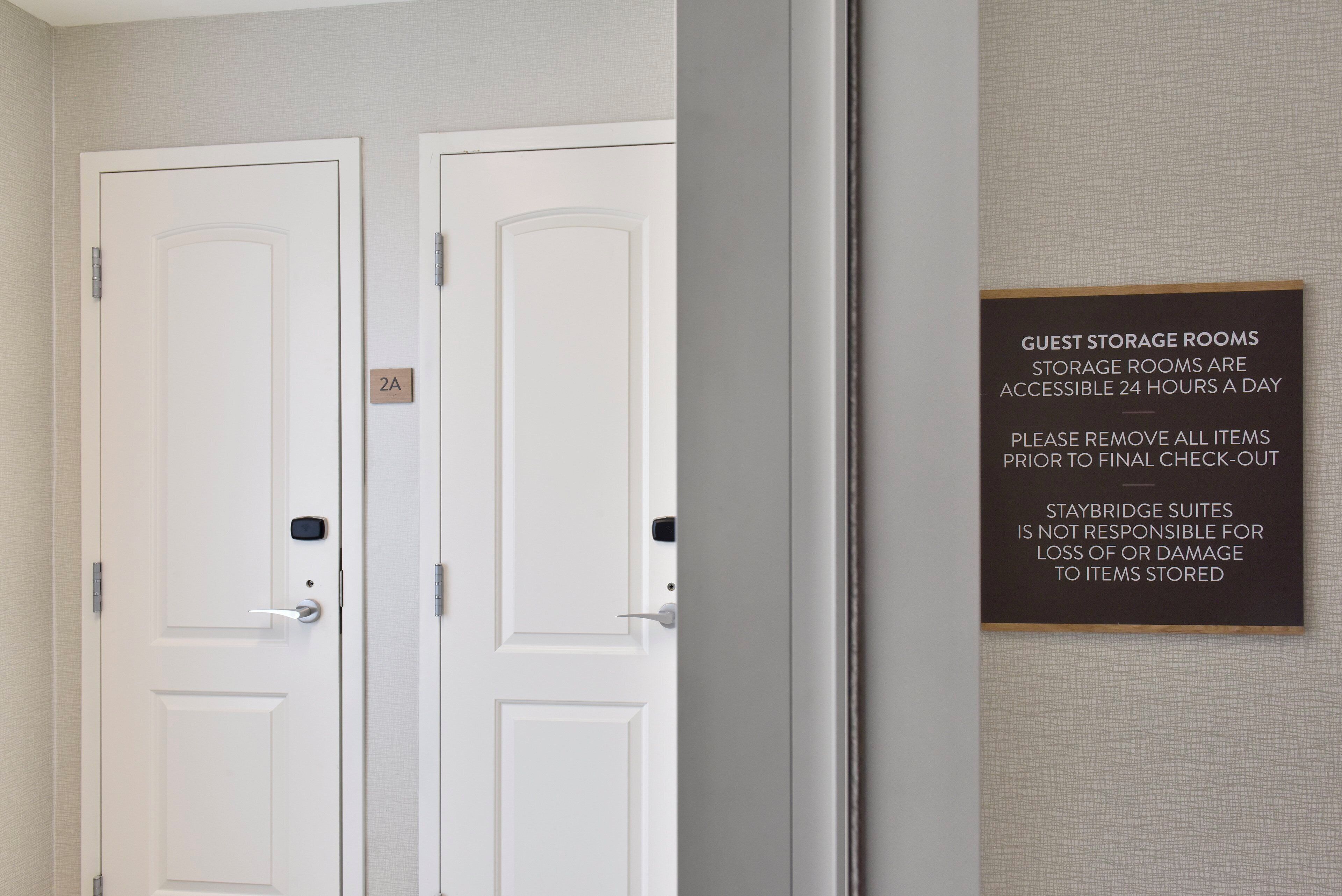A hotel room with two white doors, one labeled '2A'. A sign on the wall states that guest storage rooms are accessible 24 hours a day and advises to remove all items prior to check-out.