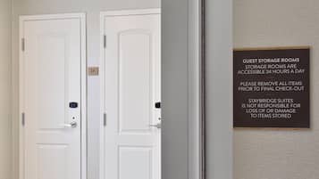 A hotel room with two white doors, one labeled '2A'. A sign on the wall states that guest storage rooms are accessible 24 hours a day and advises to remove all items prior to check-out.
