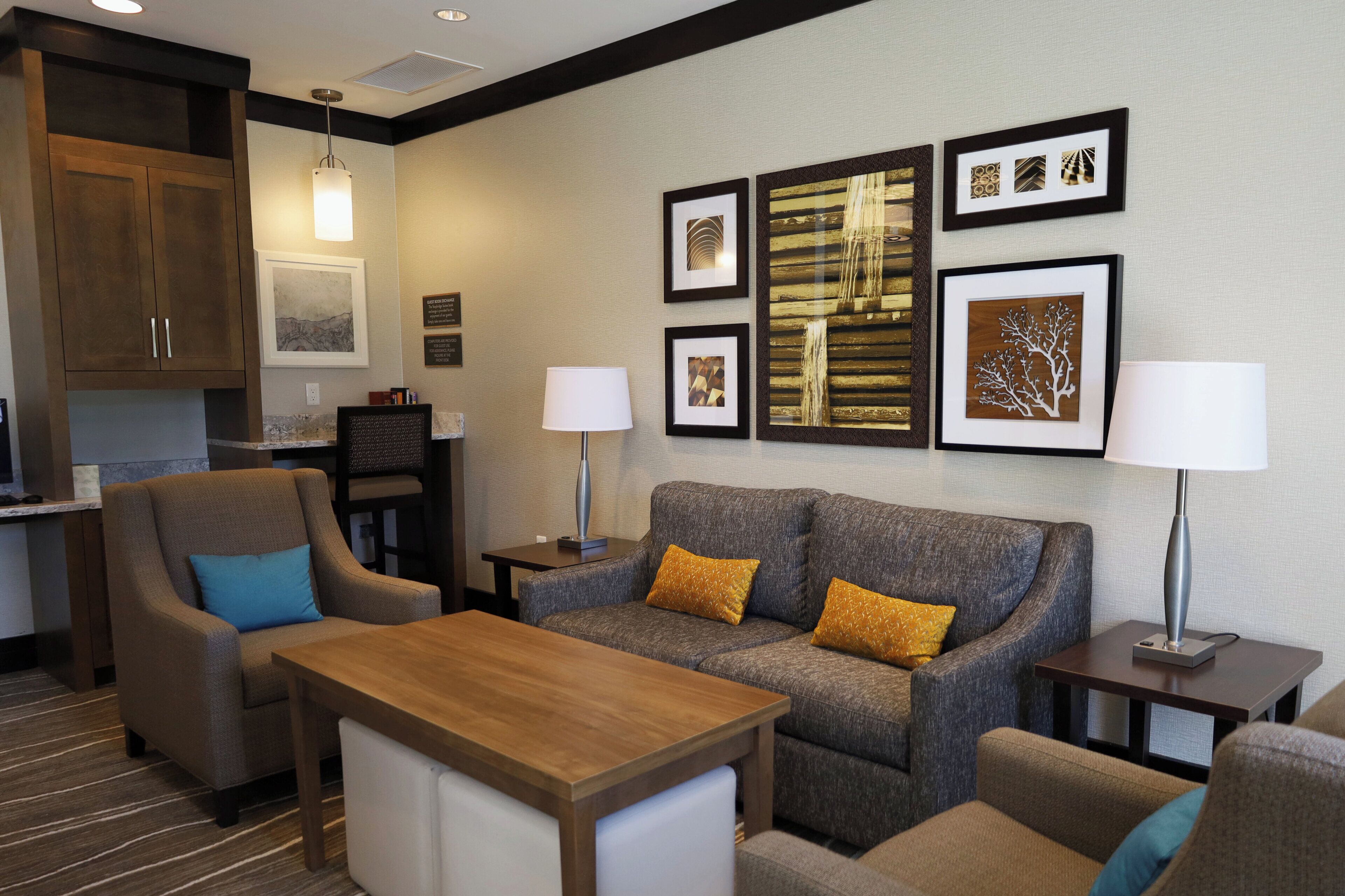 A hotel room with a sofa, armchairs, a wooden table, and a kitchen area.