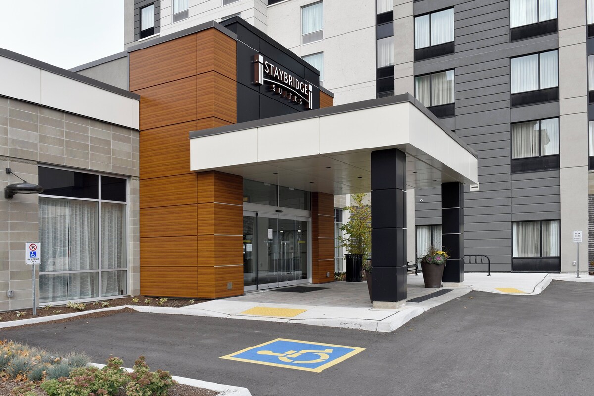 A modern hotel entrance with a covered outdoor area, a sign indicating a parking area, and a disabled parking symbol on the ground.