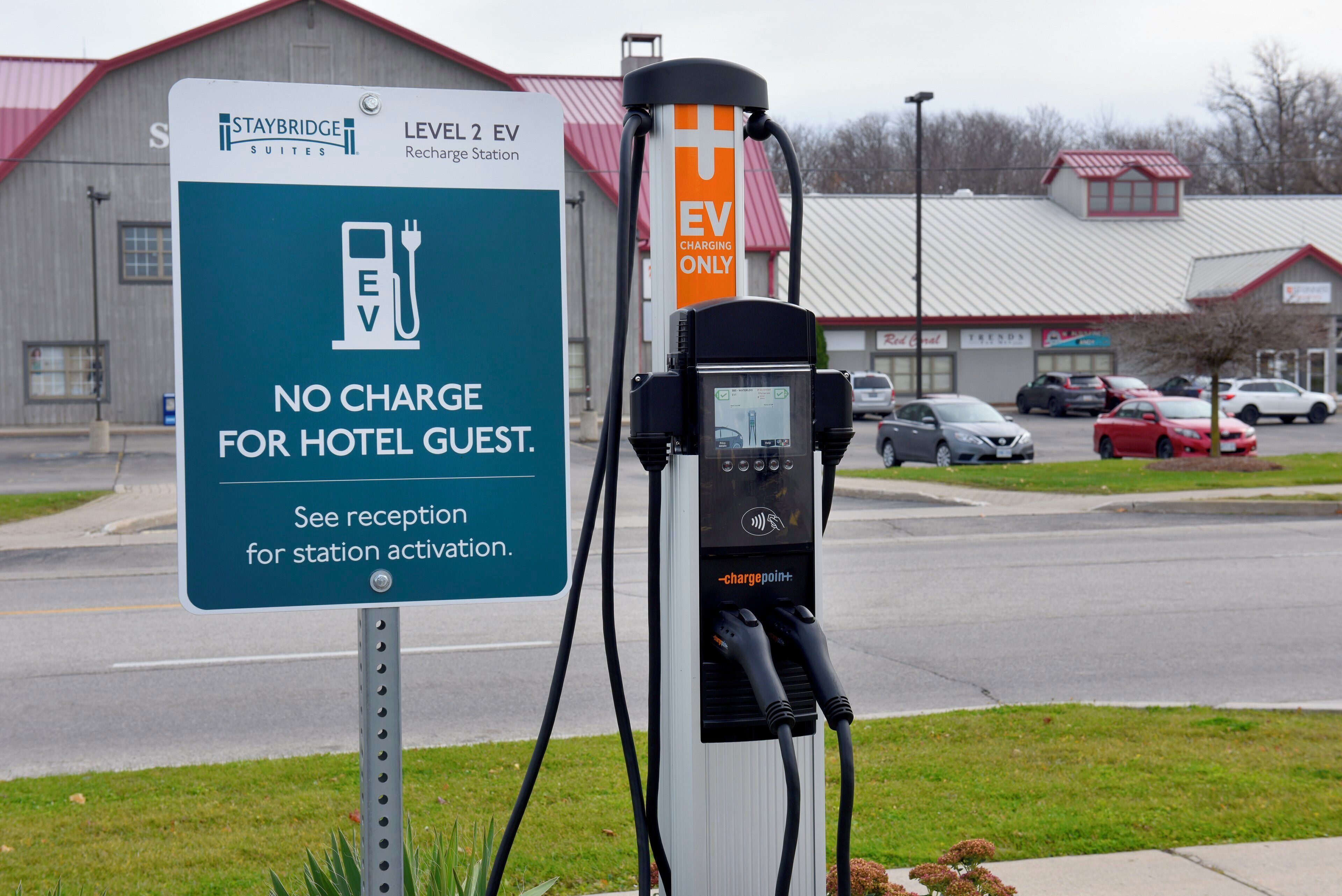 Estación de carga para vehículos eléctricos con un cartel que indica que es para huéspedes del hotel y requiere activación en recepción.