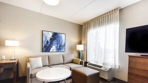 A hotel room with a sofa, ottoman, round table, TV, and artwork on the wall. - Staybridge Suites Waterloo - St. Jacobs Area by IHG (Township of Woolwich)