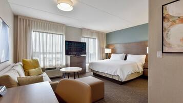 Une chambre d’hôtel avec un lit, un canapé, une petite table, une télévision et un panneau indiquant « Staybridge Suites ».