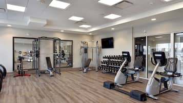 Un gimnasio con diverso equipo de ejercicio, incluyendo una estructura para sentadillas, mancuernas y máquinas de cardio.