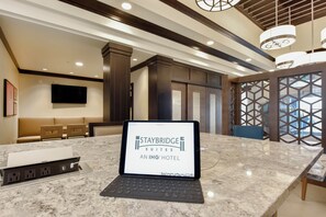 A tablet displaying Staybridge Suites An IHG Hotel branding in a hotel lobby with a marble countertop, seating area, and modern decor. - Staybridge Suites Waterloo - St. Jacobs Area by IHG (Township of Woolwich)