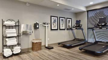 Une salle de sport équipée de deux tapis de course, d’un porte-serviettes, d’un appareil d’exercice fixé au mur et de tableaux encadrés accrochés au mur.