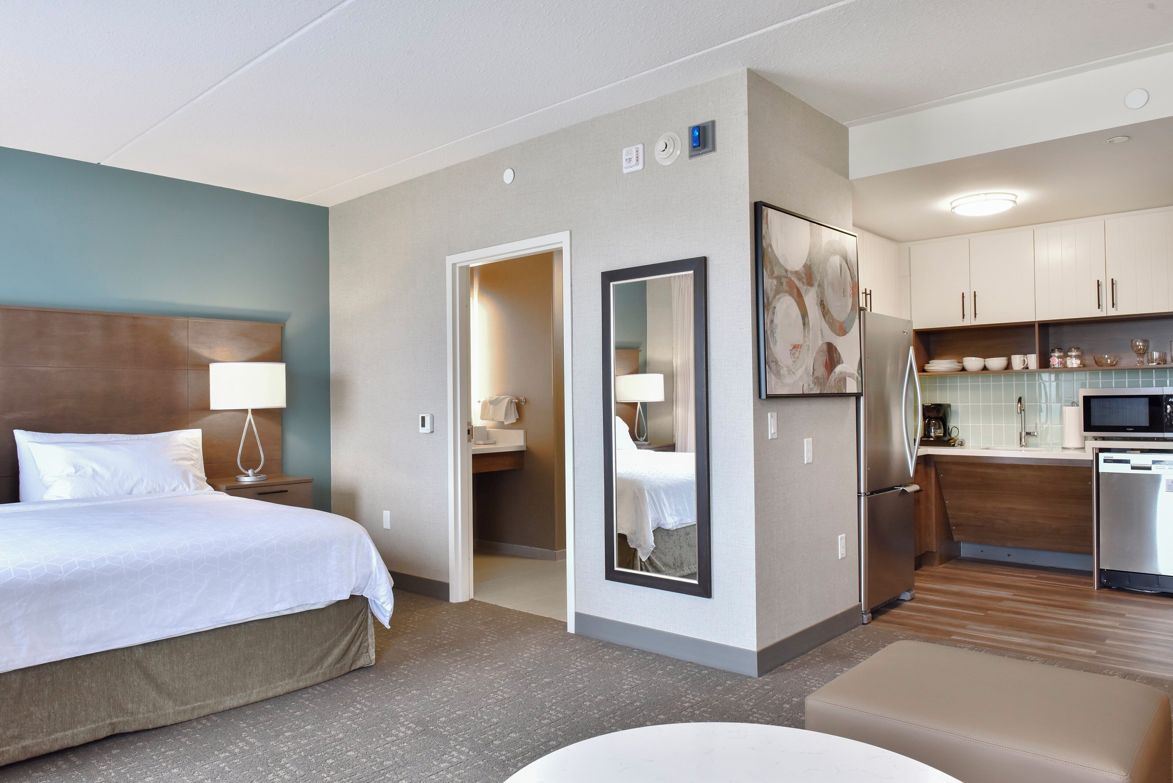 A hotel room with a bed, a bathroom, a kitchen area, and a dining table.
