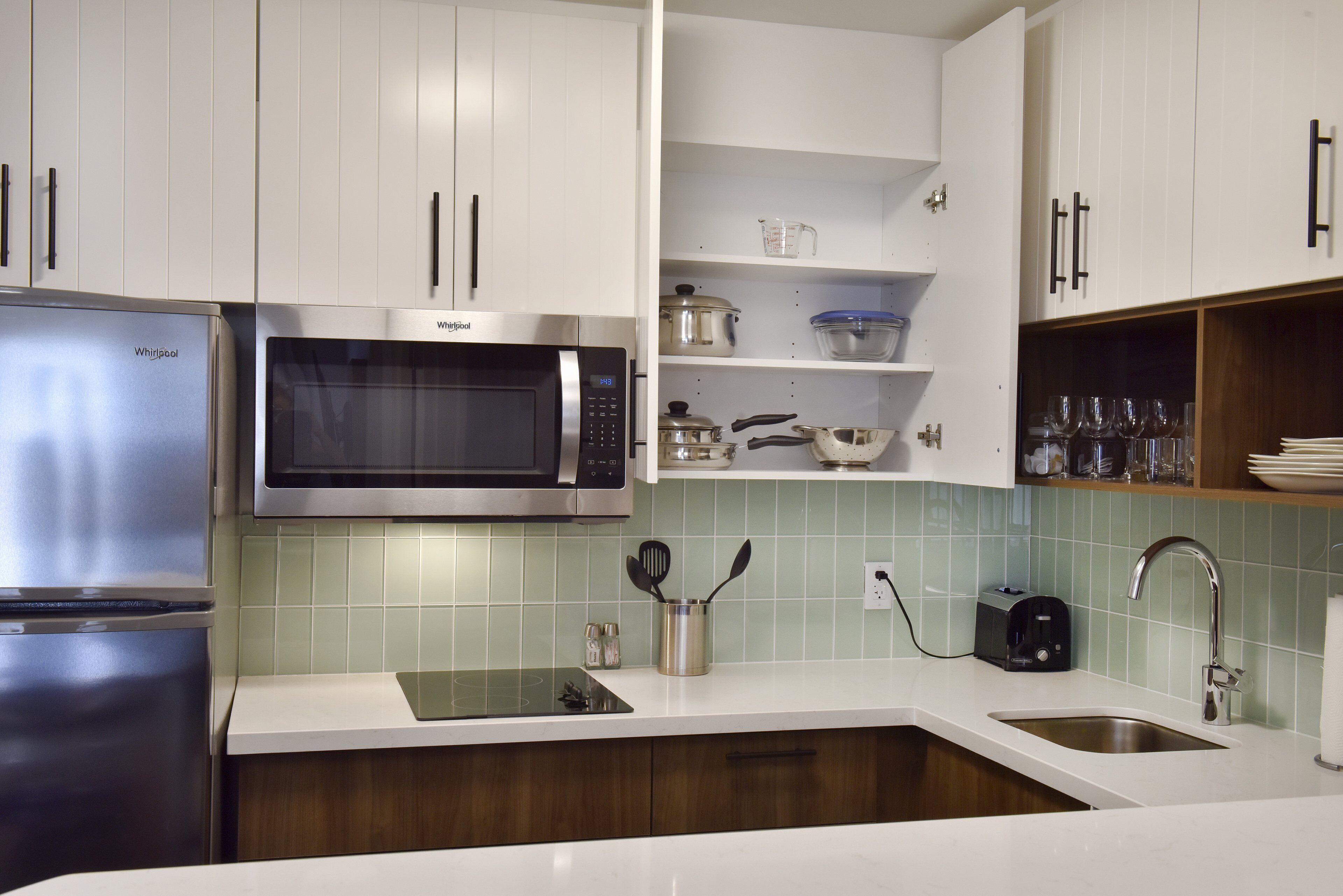 Una cocina moderna con armarios blancos, un refrigerador de acero inoxidable, un microondas y un lavamanos.