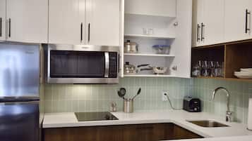 Una cocina moderna con armarios blancos, un refrigerador de acero inoxidable, un microondas y un lavamanos.