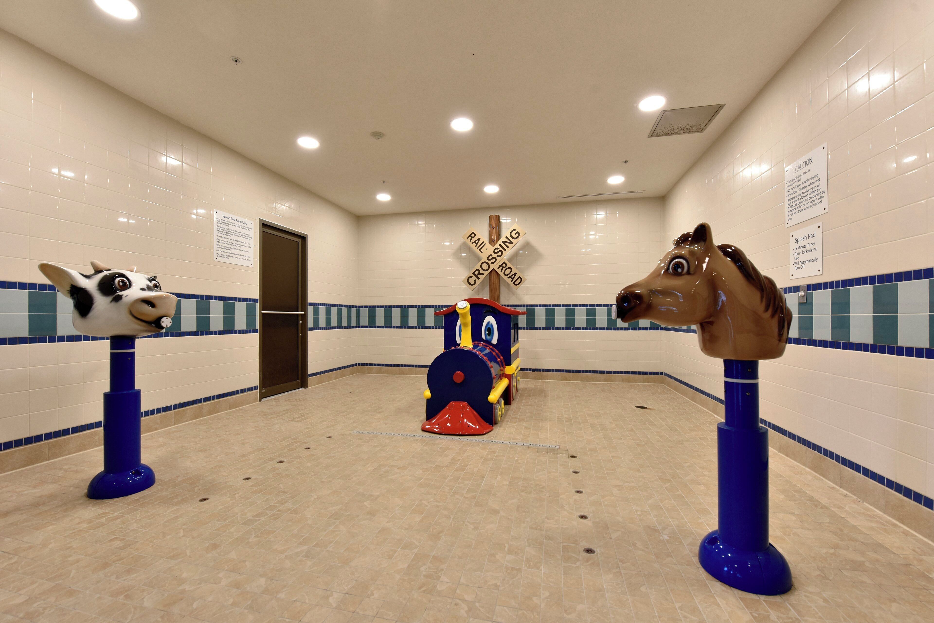 Un baño con piso de baldosas azules y blancas, un tren de juguete y dos esculturas de animales sobre pedestales.