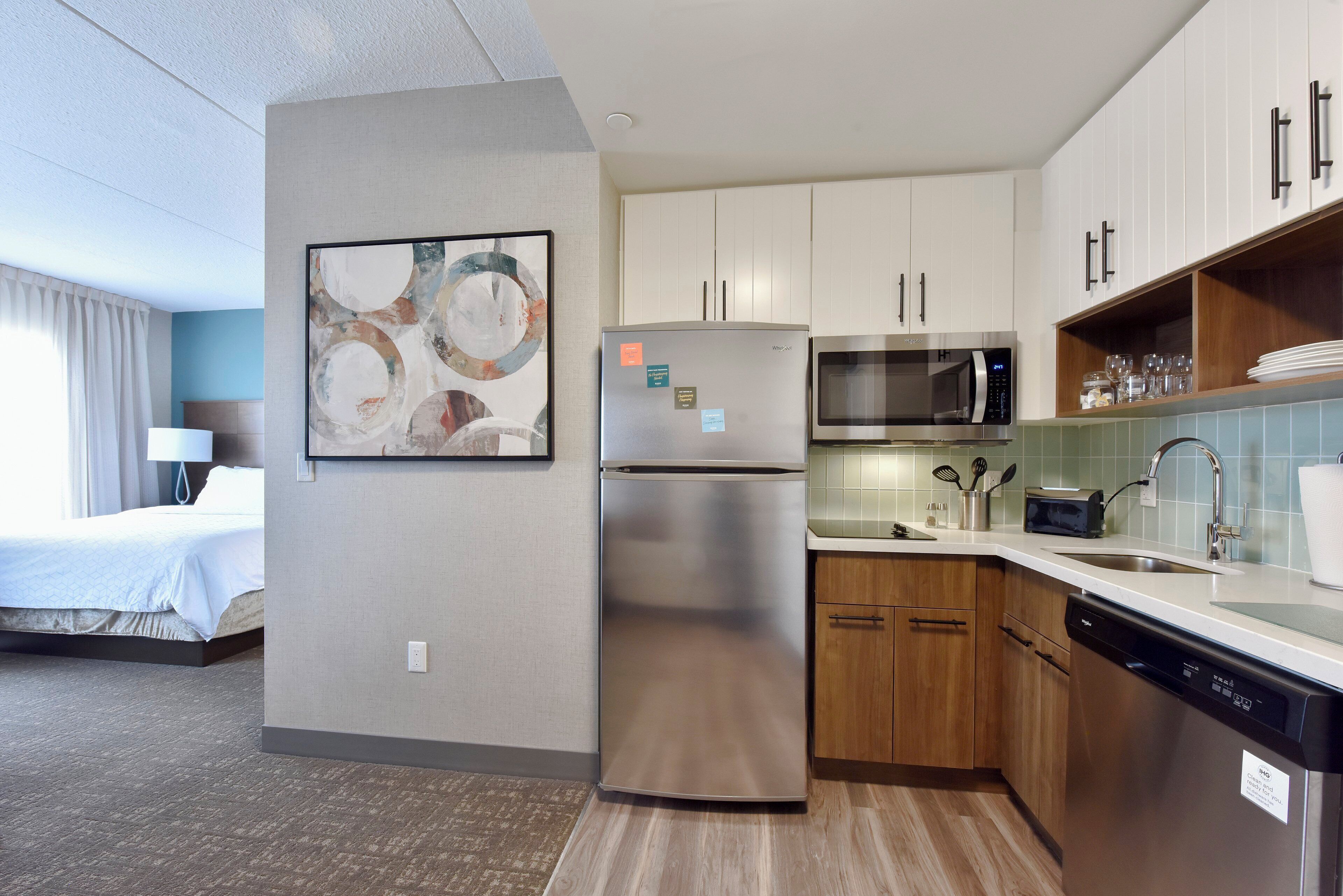 A modern hotel kitchen with stainless steel appliances, wooden cabinets, and a large abstract painting.