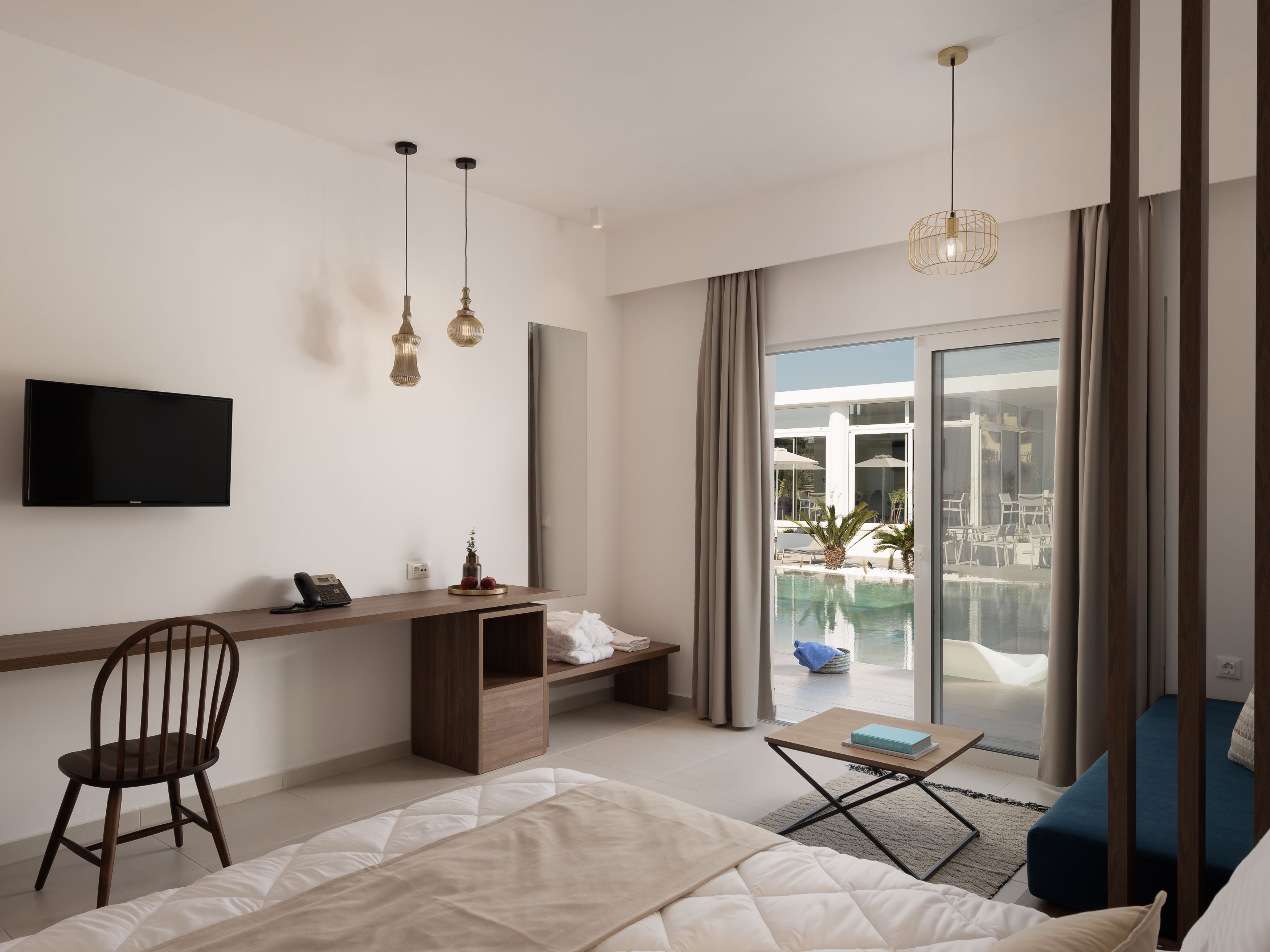 Habitación de hotel moderna con cama, escritorio, televisión y vistas a una piscina al aire libre.