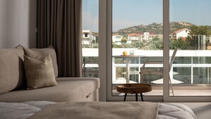 A modern hotel room with a large window, a sofa, and a small table with a glass top. - Nama Retreat (Rhodes)