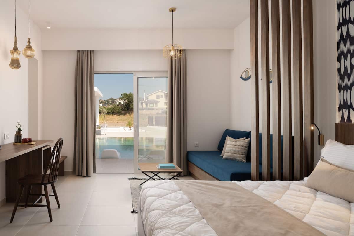 A modern hotel room with a bed, a desk, and a view of a pool and buildings.