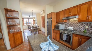 Una cucina con mobili in legno, un piano di lavoro in granito, un frigorifero in acciaio inossidabile, un forno a microonde e un piano cottura.