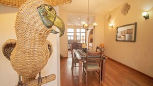 Zona pranzo con tavolo e sedie in legno, una scultura di uccello in vimini e un lampadario.