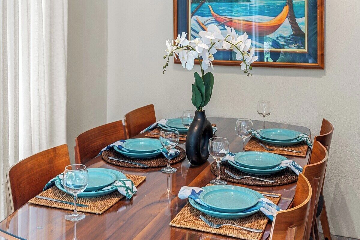 Una mesa de comedor dispuesta con platos azules, vasos y un florero con flores blancas.