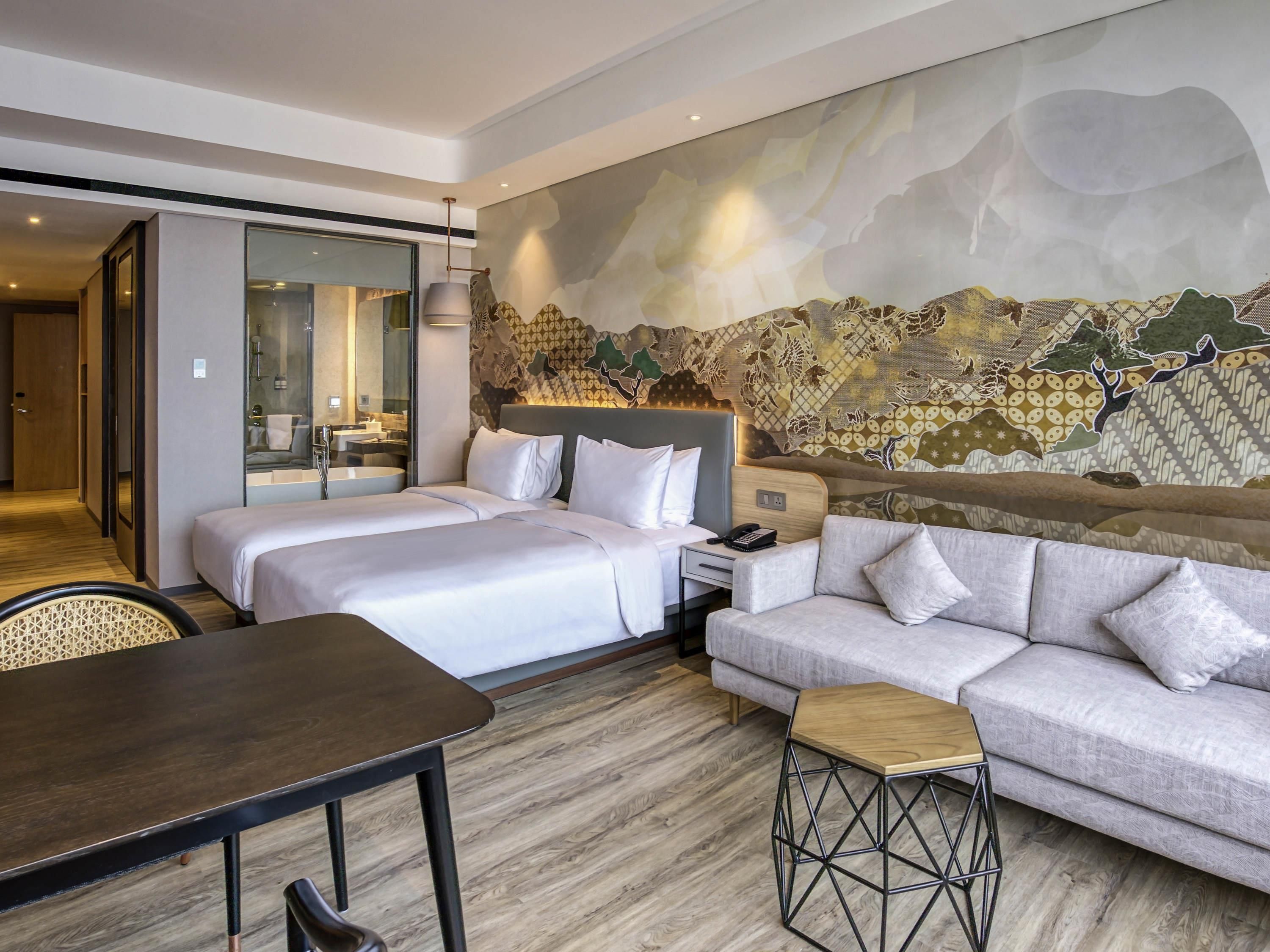 Ein Hotelzimmer mit Bett, einer Couch, einem kleinen Tisch, einem Spiegel und einer Wand mit einem dekorativen Muster.