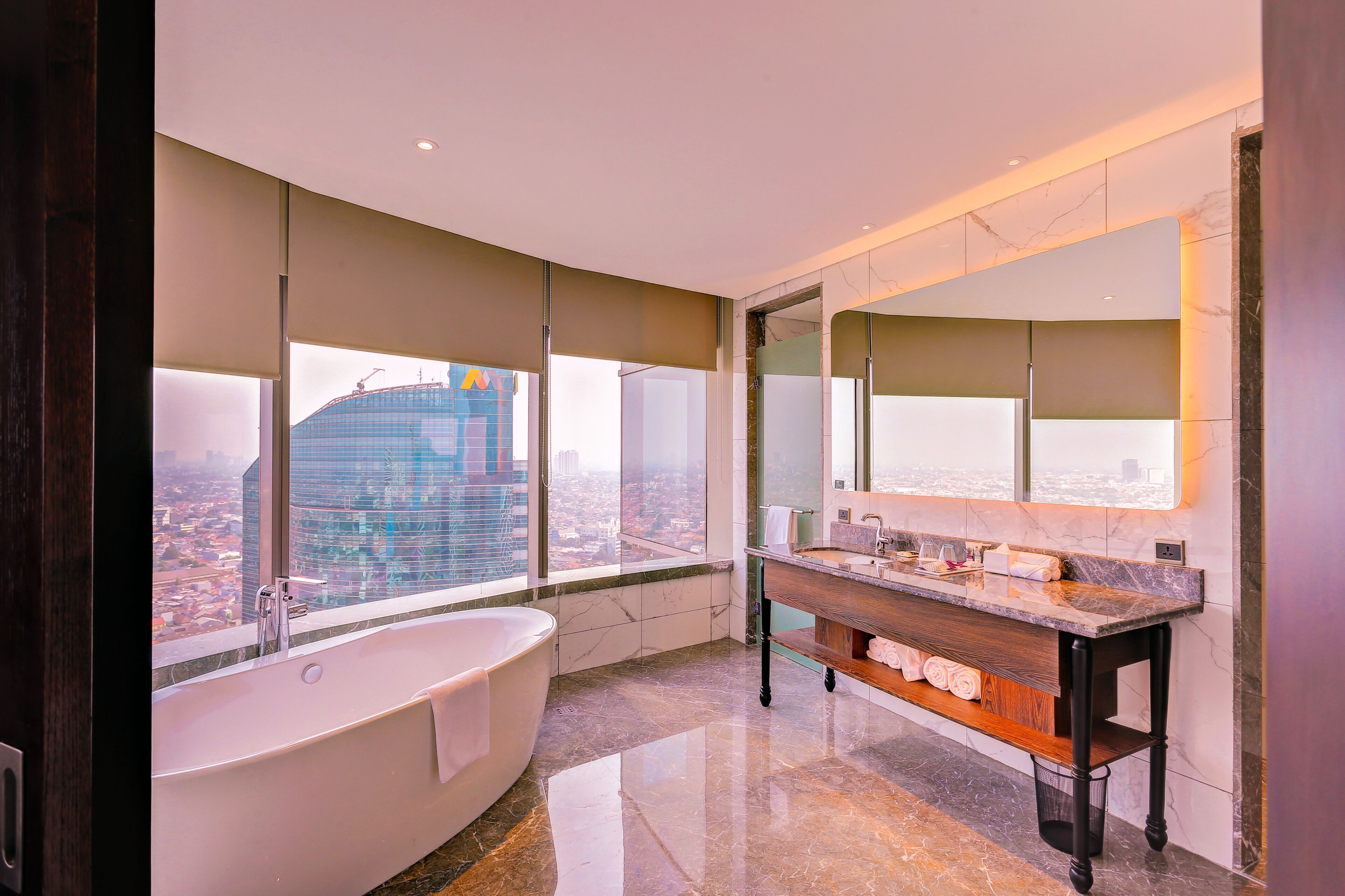 Un bagno moderno con una vasca da bagno ampia, un mobile lavabo con specchio e vista sulla città attraverso ampie finestre.