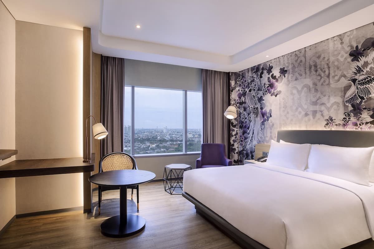 Ein Hotelzimmer mit Bett, Schreibtisch, Stuhl, einem kleinen Tisch und Blick auf die Stadt.