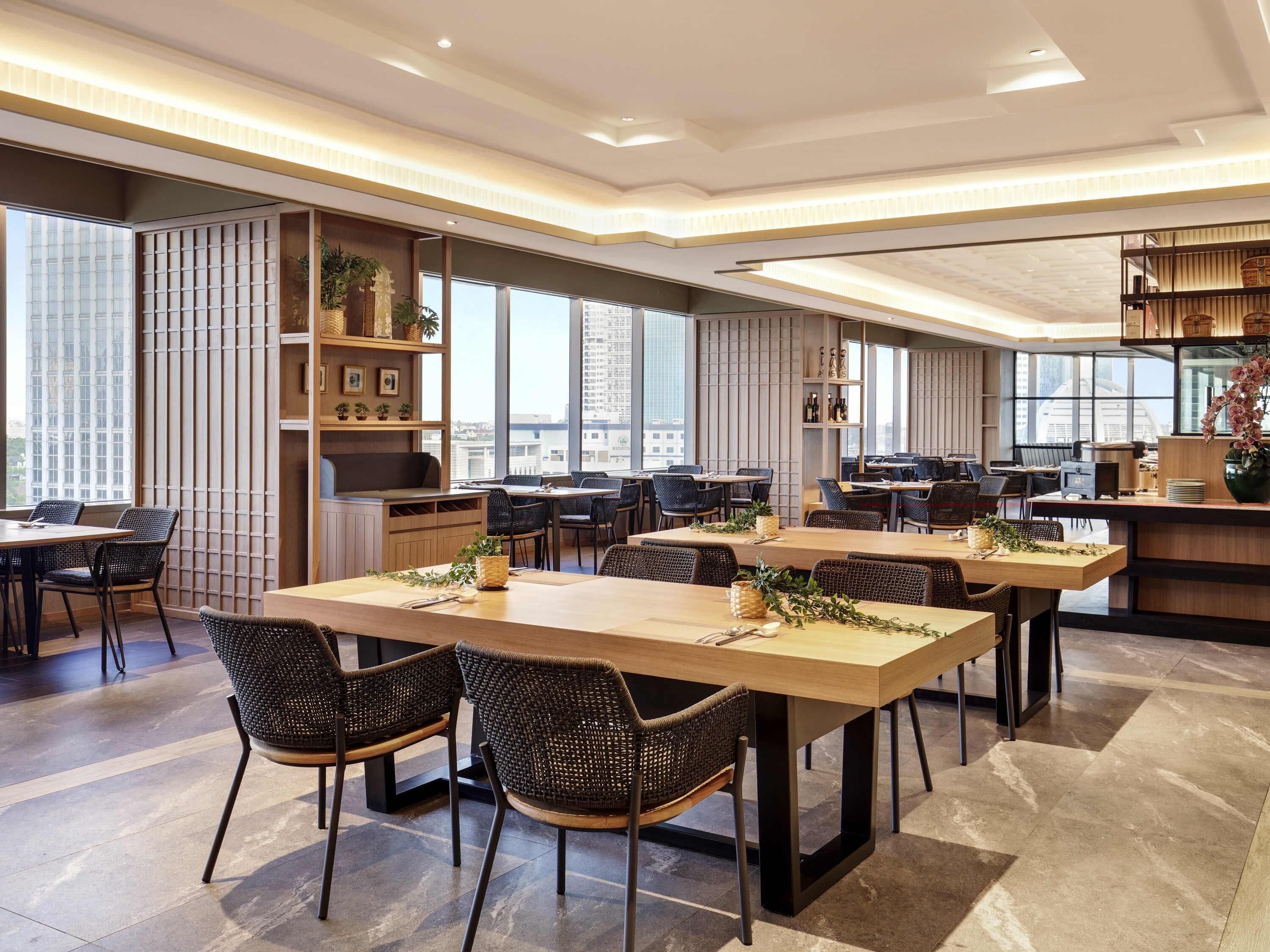 A modern dining area with long tables, chairs, and a view of the cityscape.