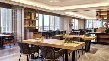 A modern dining area with long tables, chairs, and a view of the cityscape.