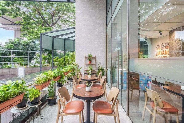 Een modern buitenzitgedeelte met ronde tafels en stoelen, omgeven door potplanten en glazen wanden.