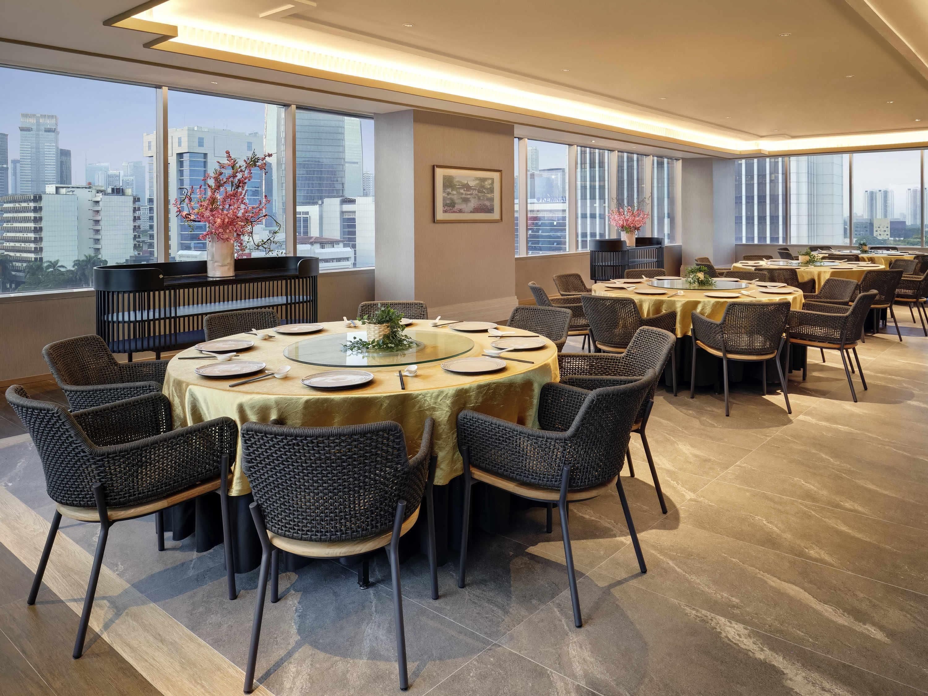 A modern dining area with round tables, wicker chairs, and a city view.