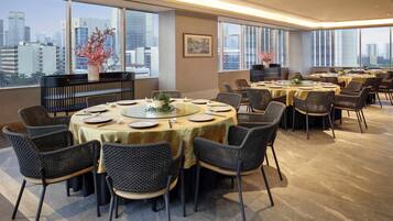 A modern dining area with round tables, wicker chairs, and a city view.