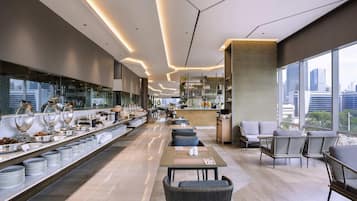 A modern hotel lobby with a long reception desk, seating area, and a bar.