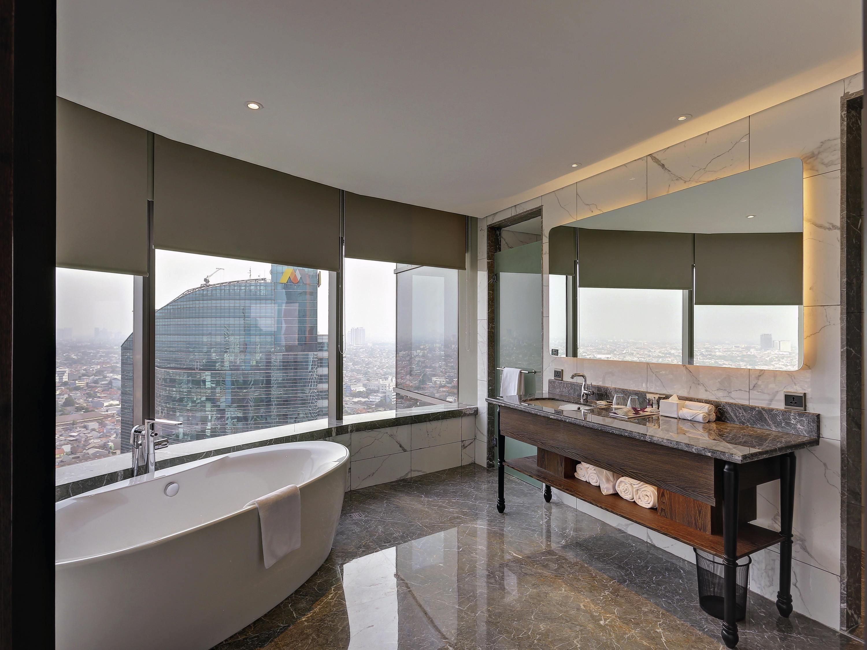A modern bathroom with a large bathtub, a vanity with a mirror, and a city view.