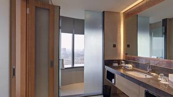 Une salle de bain moderne avec un grand miroir, deux lavabos, une douche et une vue sur la ville.