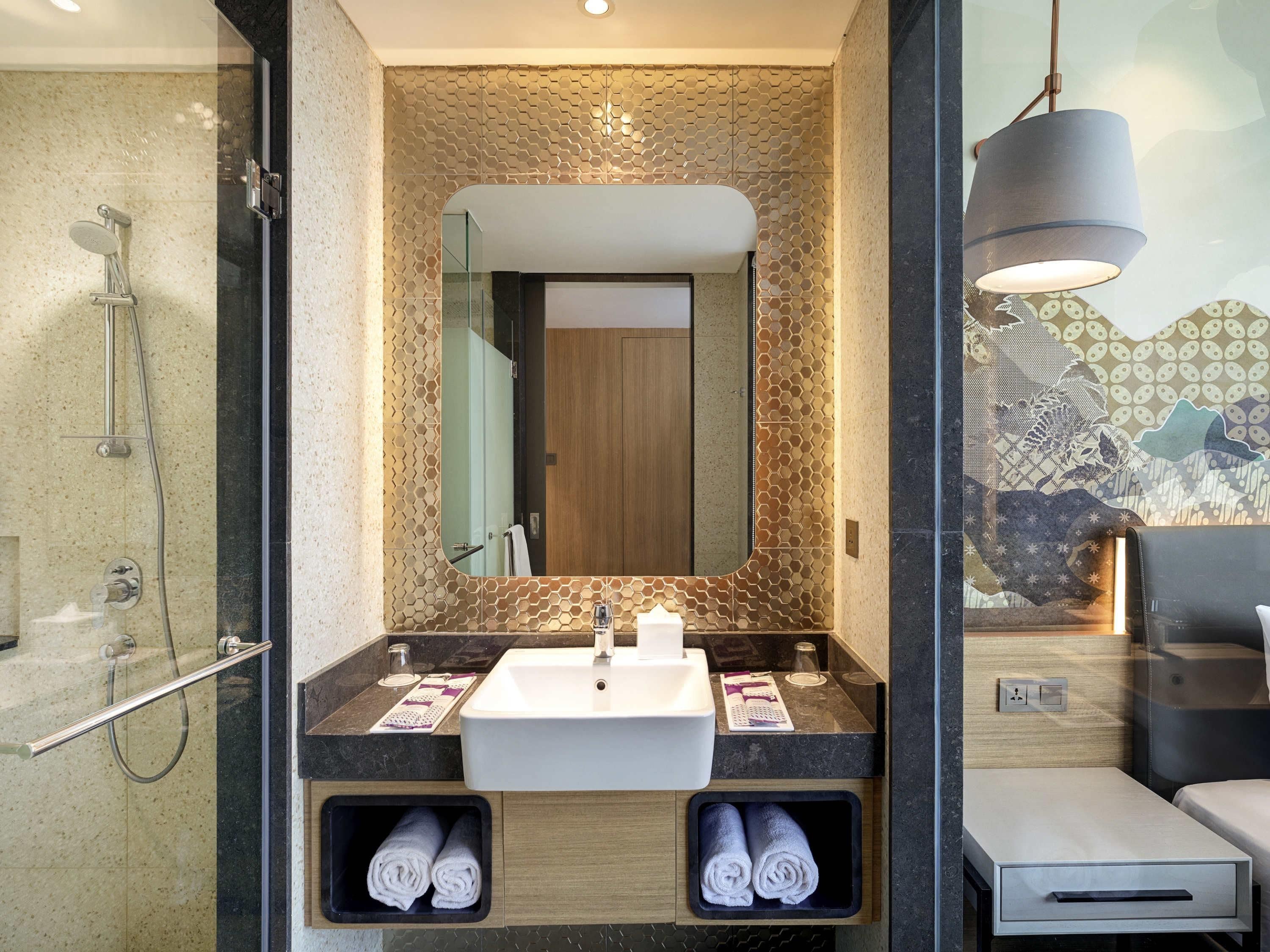 Une salle de bain moderne dotée d’une douche à parois de verre, d’un grand miroir et d’un lavabo muni de deux supports pour les serviettes.