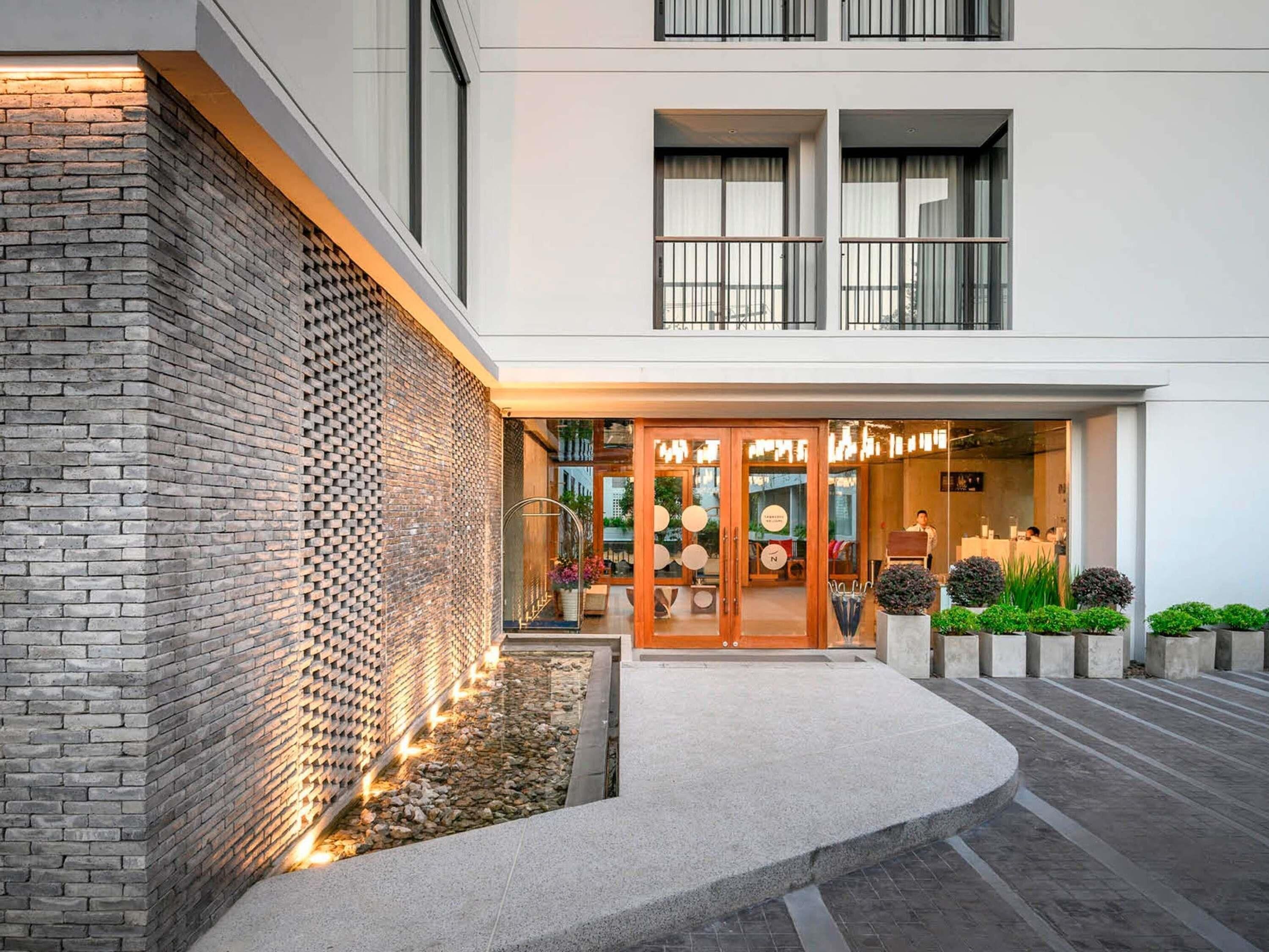 Een hotelgevel van baksteen, een glazen entree en een klein terras met planten.