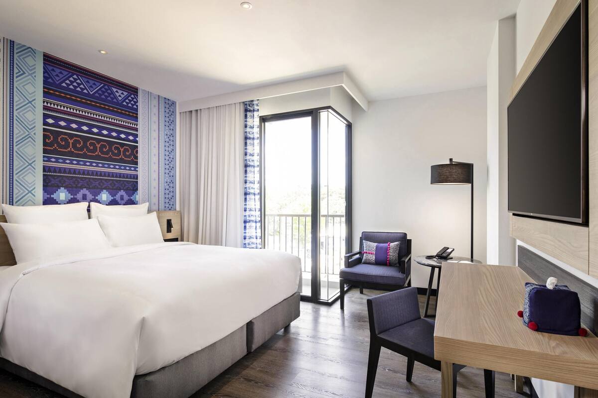 Une chambre d’hôtel avec un grand lit, un bureau avec une chaise, une télévision et un balcon avec des rideaux.