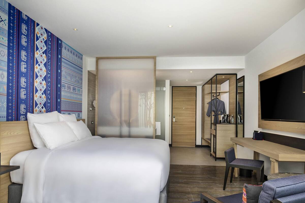 Une chambre d’hôtel moderne équipée d’un grand lit, d’un bureau, d’une chaise, d’une télévision et d’une armoire.