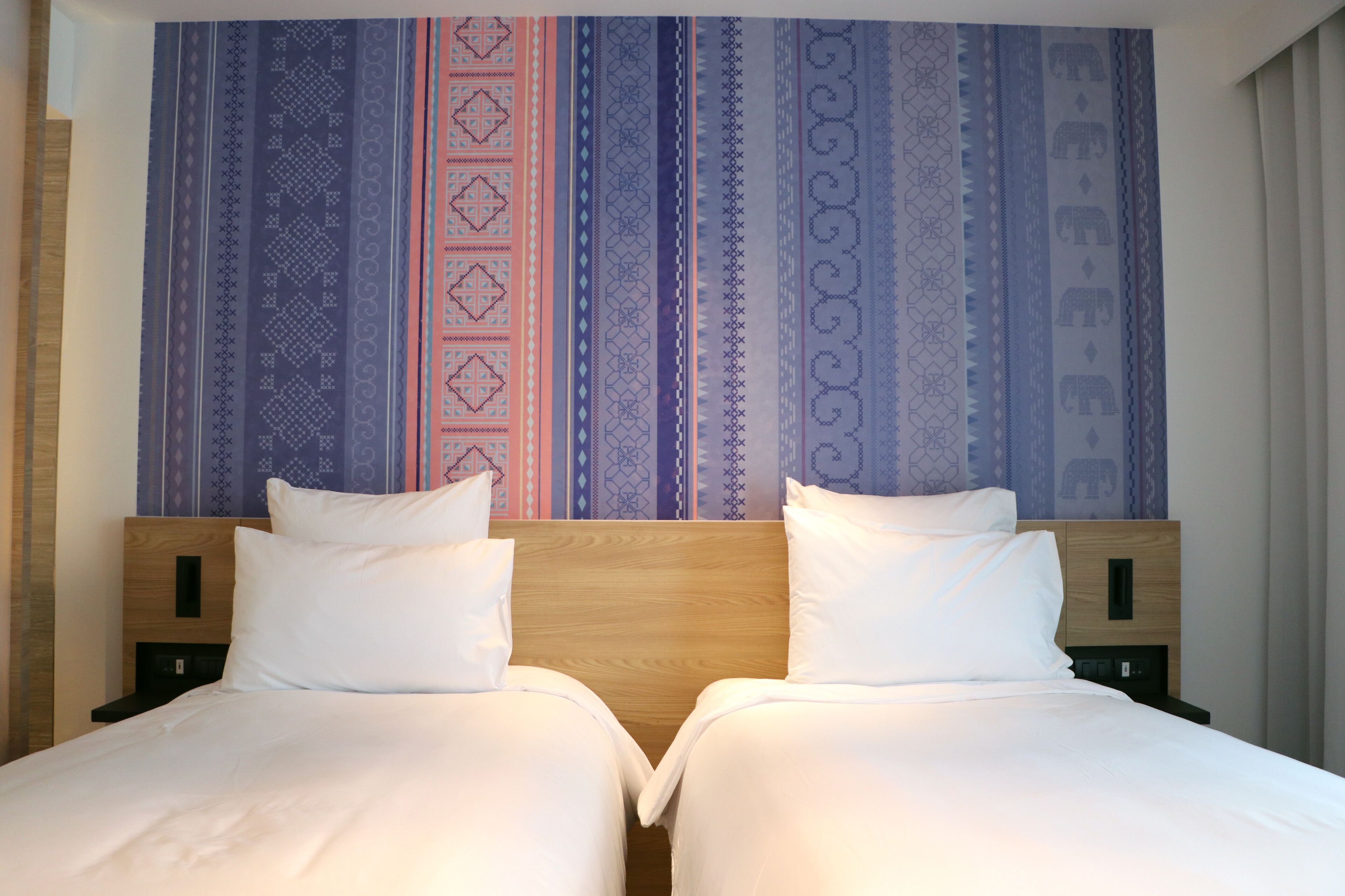 Habitación de hotel con dos camas, cabecero de madera y un tapiz grande con diseño.
