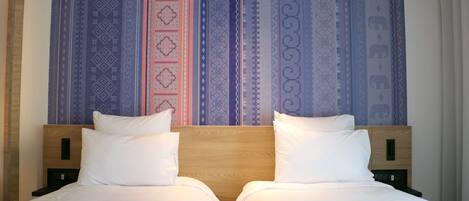 Habitación de hotel con dos camas, cabecero de madera y un tapiz grande con diseño.