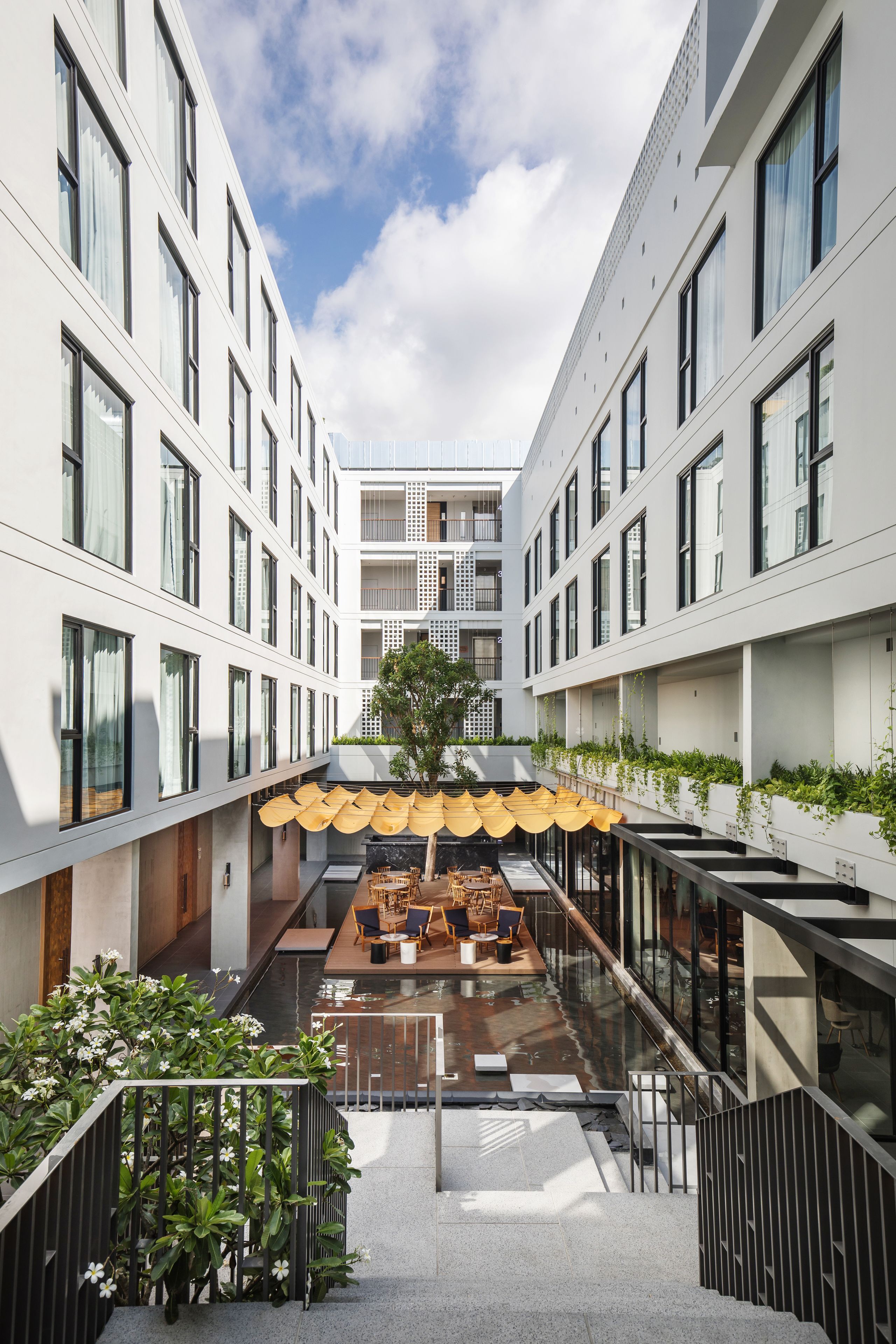 A modern hotel atrium with a central seating area, glass railings, and a view of the sky.