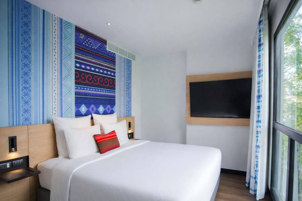 Une chambre d’hôtel moderne dotée d’un grand lit, d’un téléviseur à écran plat et d’une fenêtre avec des rideaux.