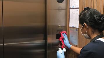 A person cleaning an elevator door with a red cloth and a spray bottle.