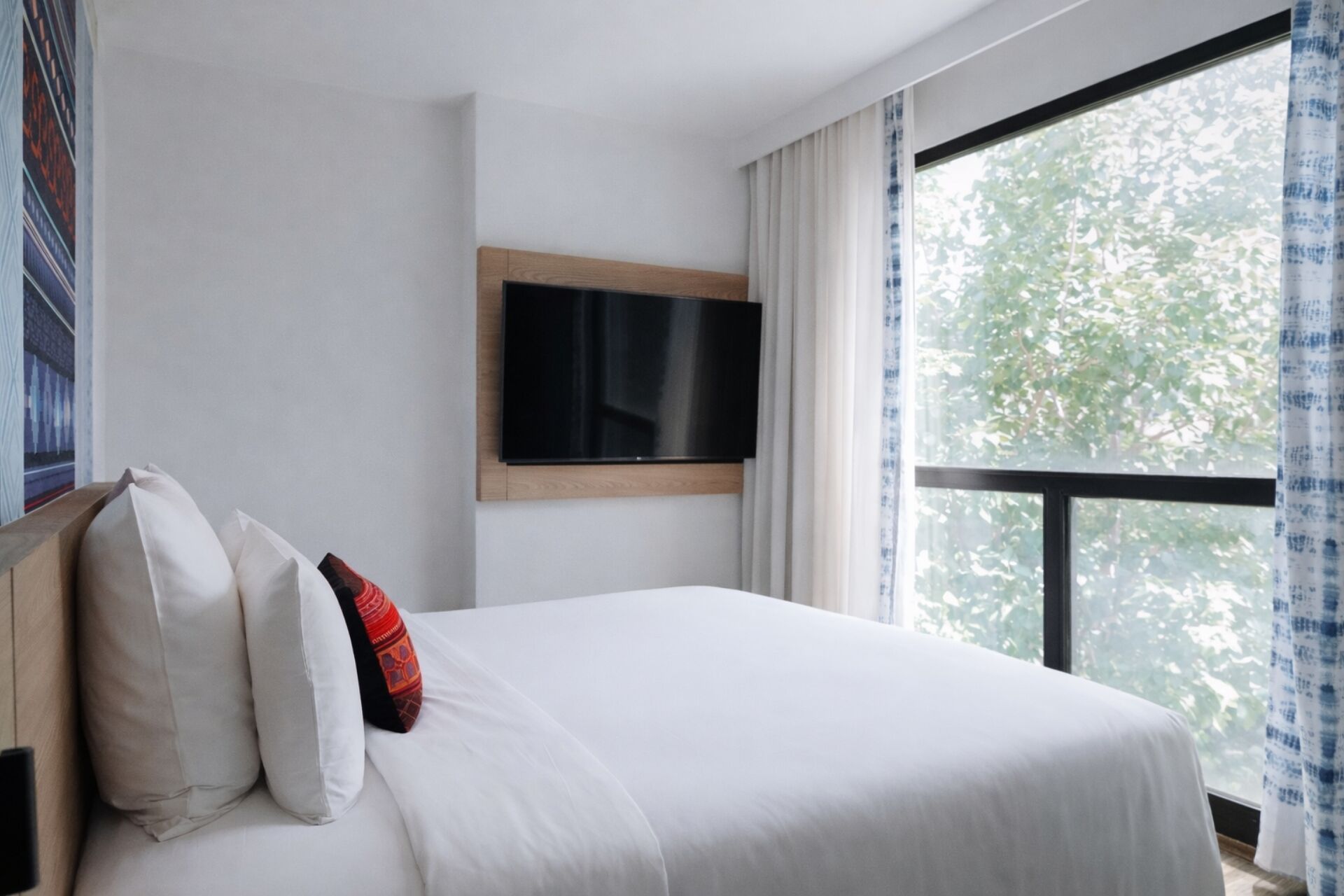 Une chambre d’hôtel avec un lit, un téléviseur à écran plat fixé au mur et une grande fenêtre avec des rideaux.