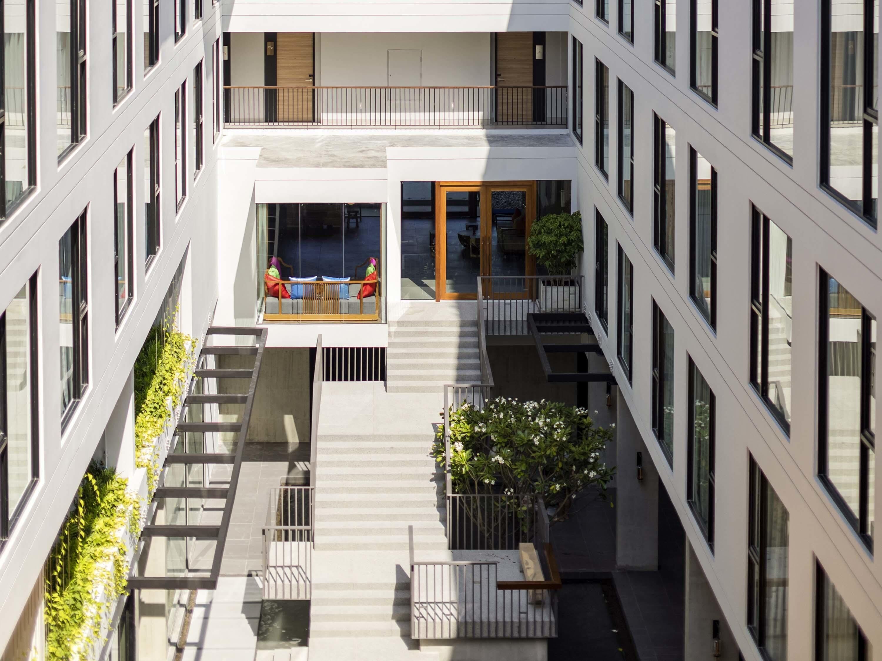 Een modern gebouw met meerdere verdiepingen, grote ramen en een centrale binnentuin met zitplaatsen en planten.