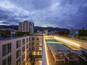 A rooftop pool area with lounge chairs, a pool, and a view of surrounding buildings and mountains. - Novotel Chiangmai Nimman Journeyhub (Chiang Mai)